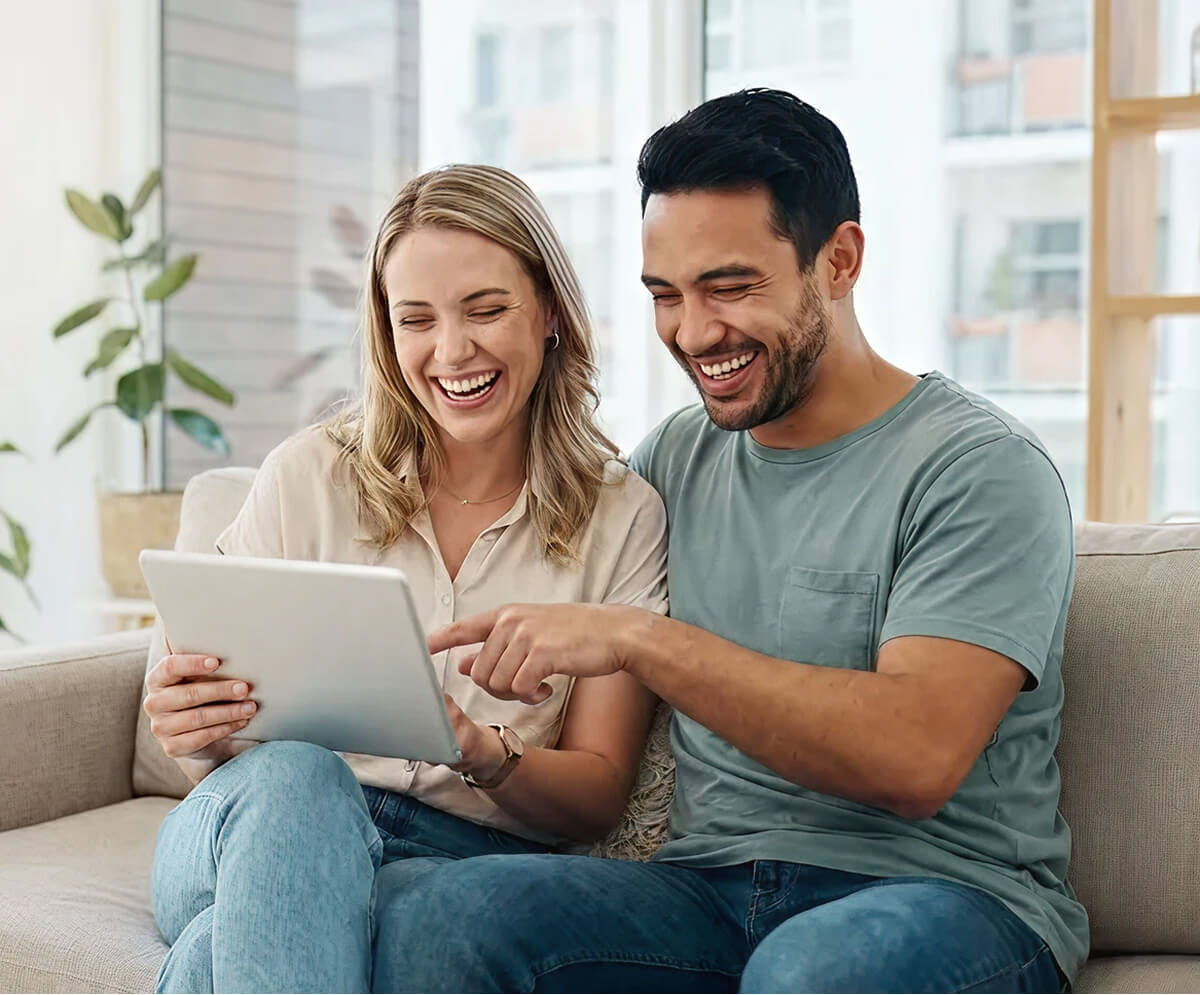 Couple souriant utilisant une tablette sur canapé